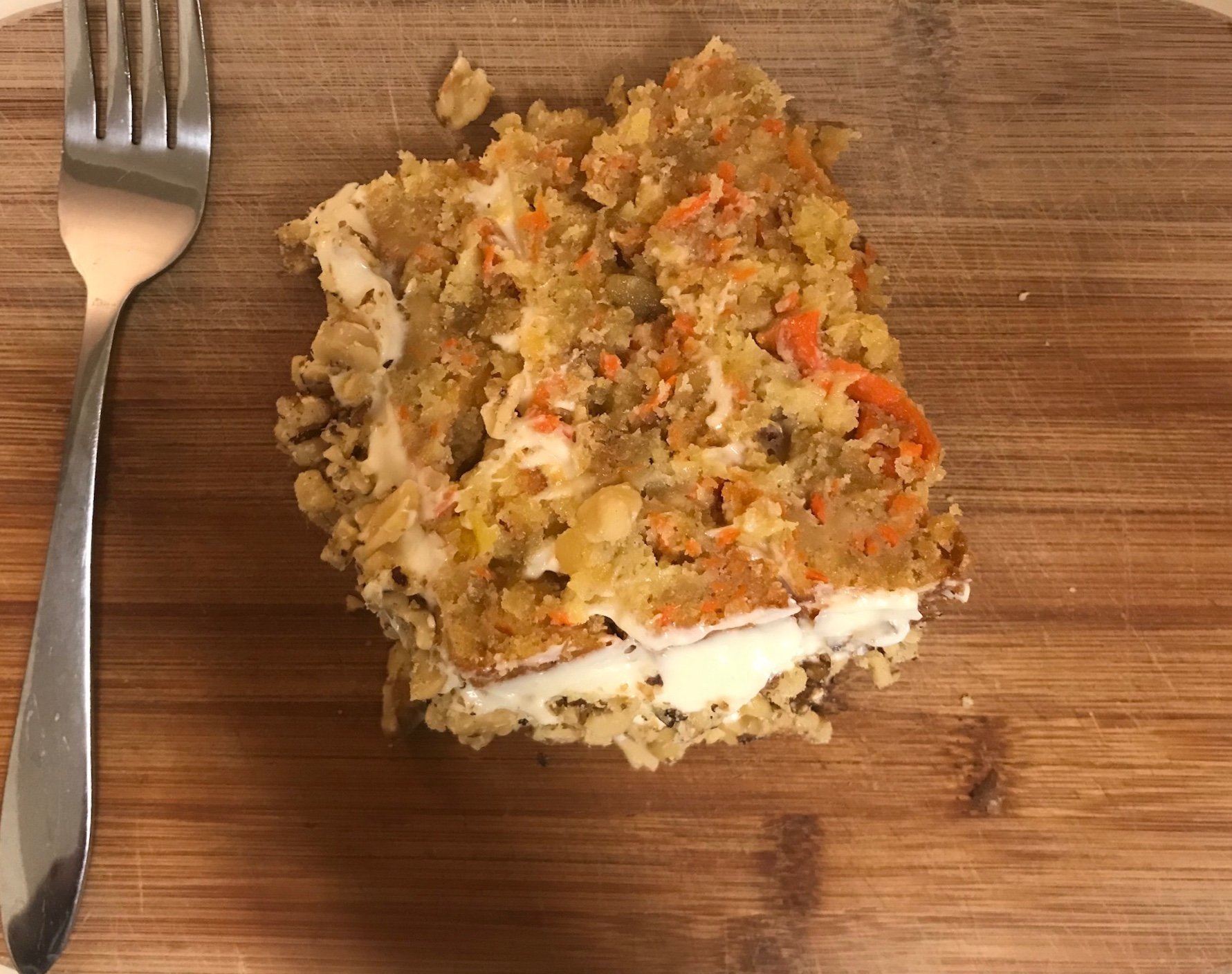 A slice of carrot cake with cream cheese frosting on a wooden board
