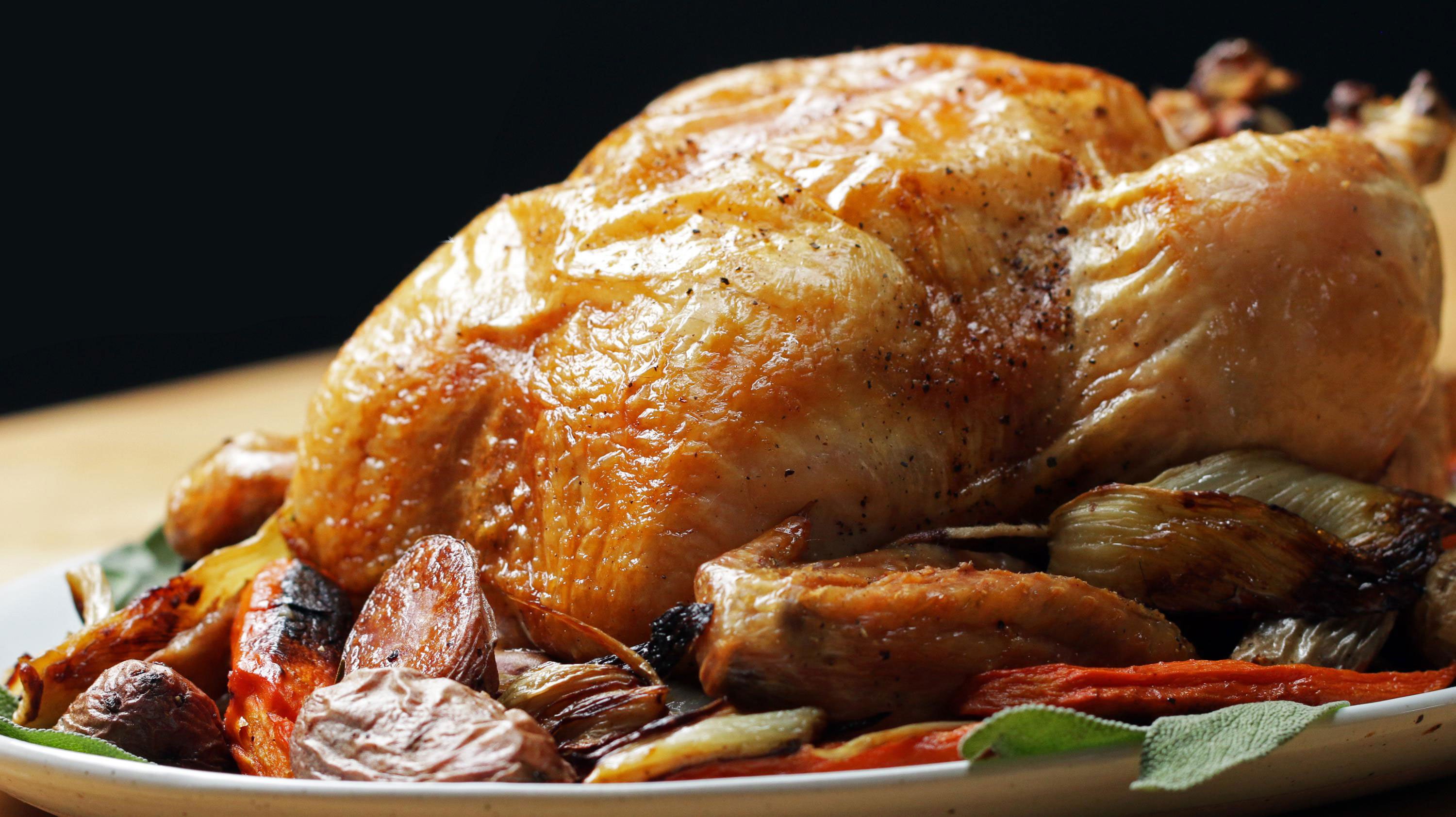 A whole golden roast chicken on a serving platter with vegetables